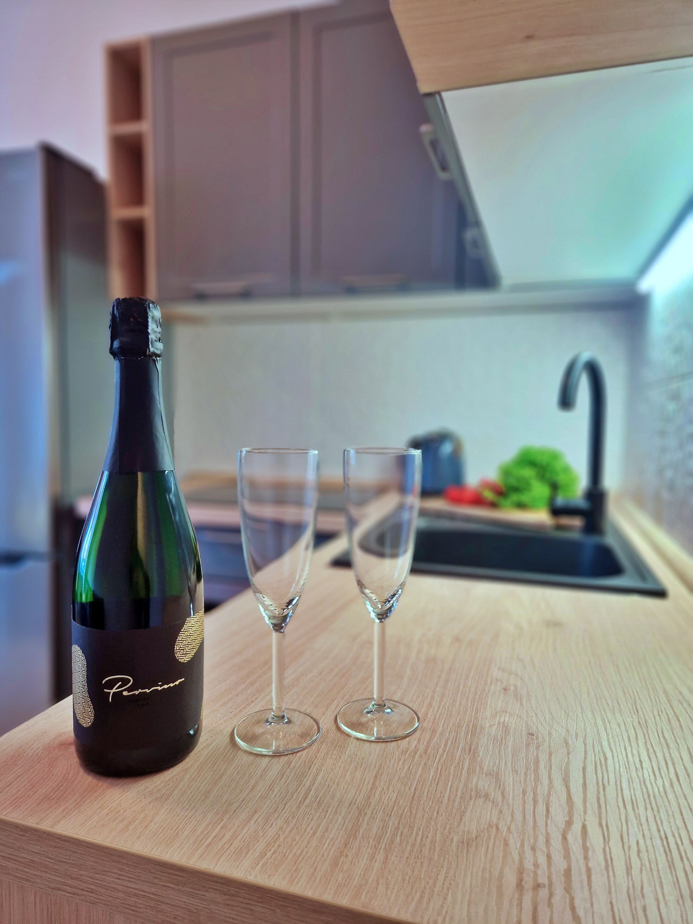 A bottle of wine and two glasses on a wooden countertop in a kitchen.