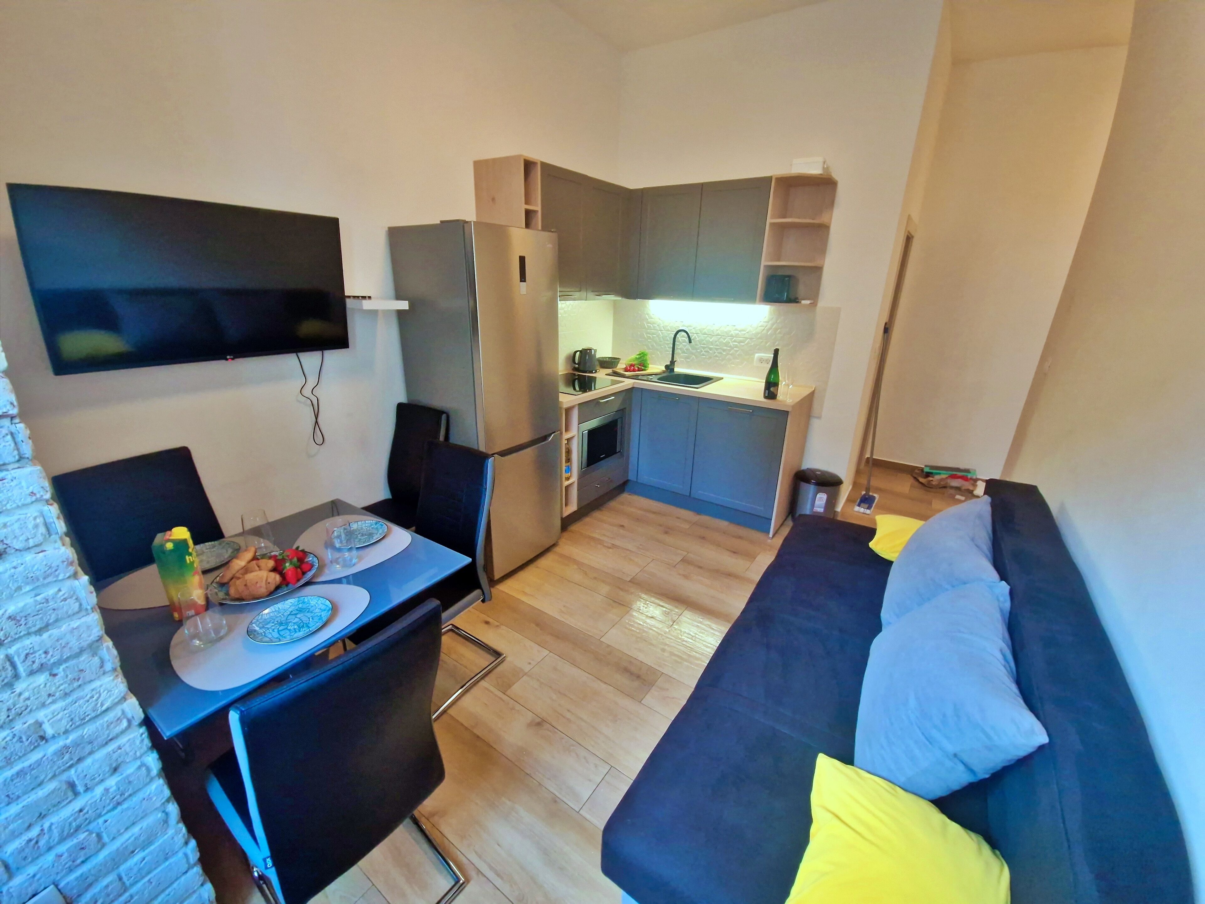 Un espacio habitable compacto con kitchenette, una zona de comedor con mesa y sillas, y un sofá con cojines.