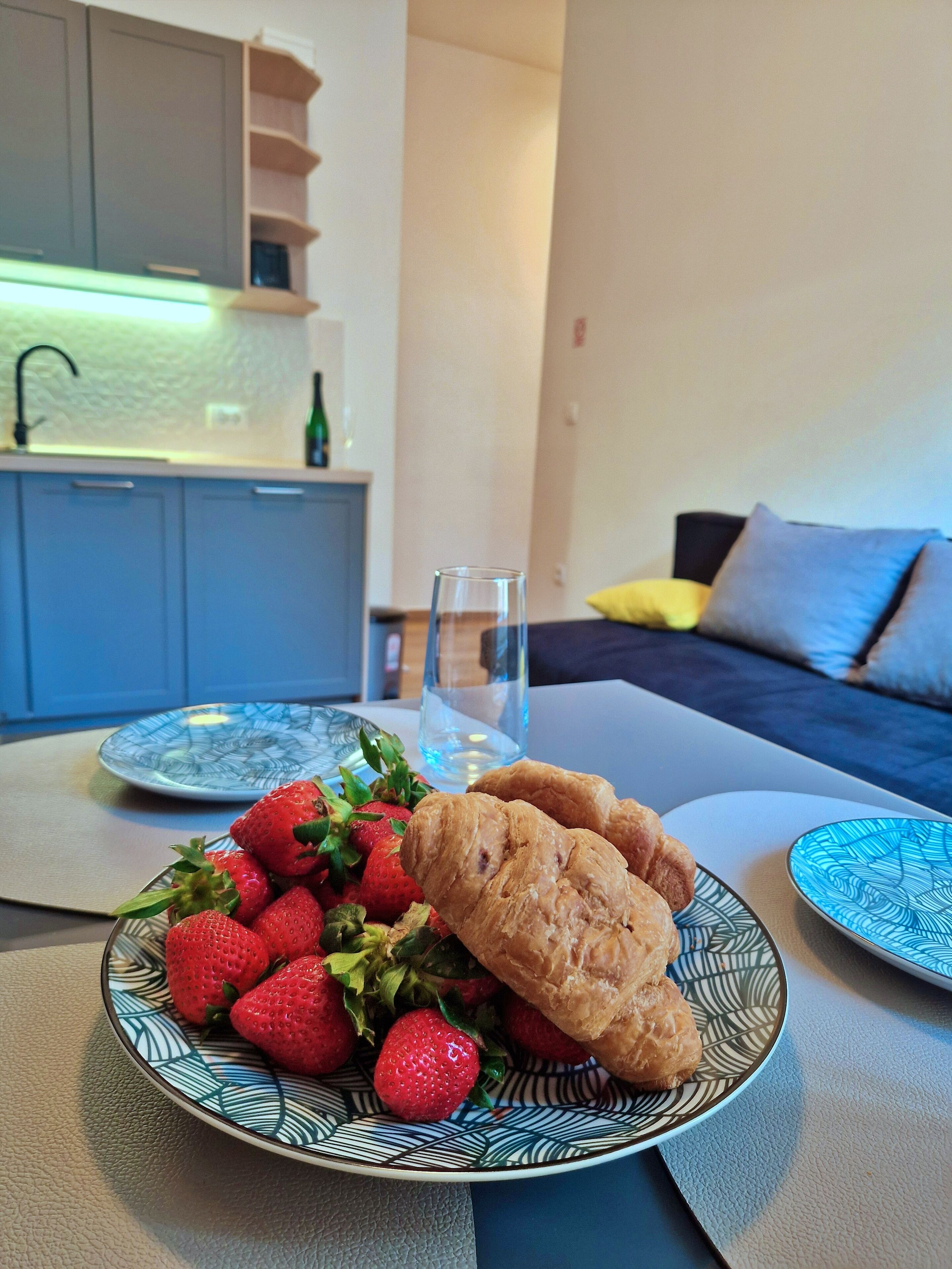 A dining table with a plate of strawberries and croissants, a glass of water, and a blue patterned plate.