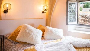 Ein Schlafzimmer mit Gewölbedecke, einem Bett mit weißer und gelber Bettwäsche, zwei Wandleuchten und einem Fenster mit Blick nach draußen.