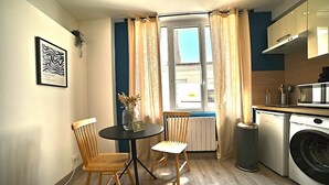 A compact kitchen with a washing machine, a small table with chairs, and a window with curtains. - L'escapade Fourasine - Heart of Fouras (Fouras)