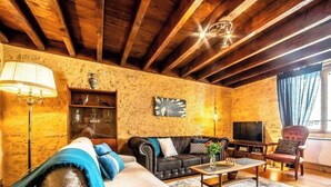 Een gezellige woonkamer met een houten plafond, een bank, een bijzettafeltje, een televisie en een boekenkast.
