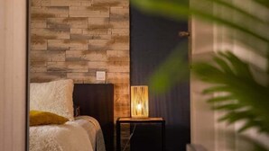 A bedroom with a stone-patterned wall, a bedside lamp, and a bed with white bedding. - Le Sarladais - Air conditioning and parking (Sarlat-la-Canéda)
