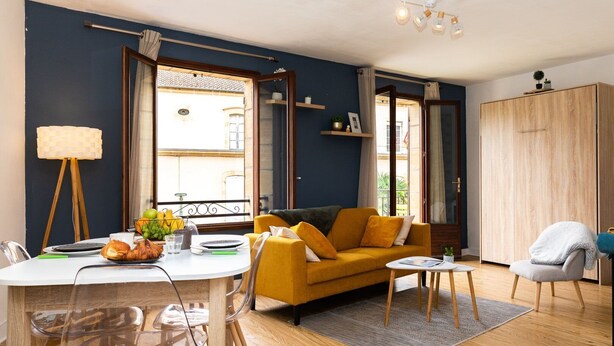 A modern living room with a yellow sofa, a dining table with chairs, a lamp, and a view of the outside. - Le Sarladais - Air conditioning and parking (Sarlat-la-Canéda)
