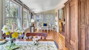 A cozy room with large windows, a wooden cabinet, and a dining area with a table set for two.