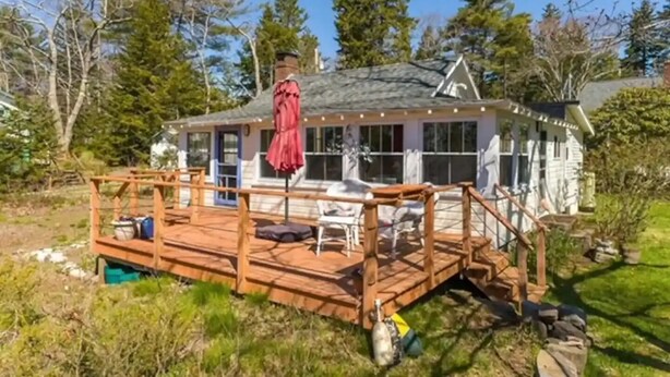 A wooden deck with outdoor furniture, a covered area with a red umbrella, and a house with large windows.