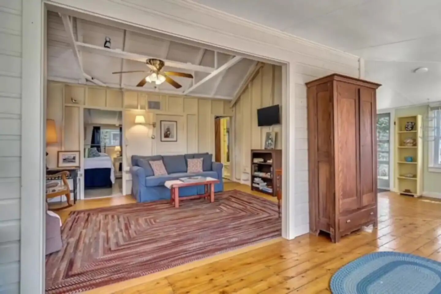 A spacious living room with a blue sofa, wooden floor, and a ceiling fan.