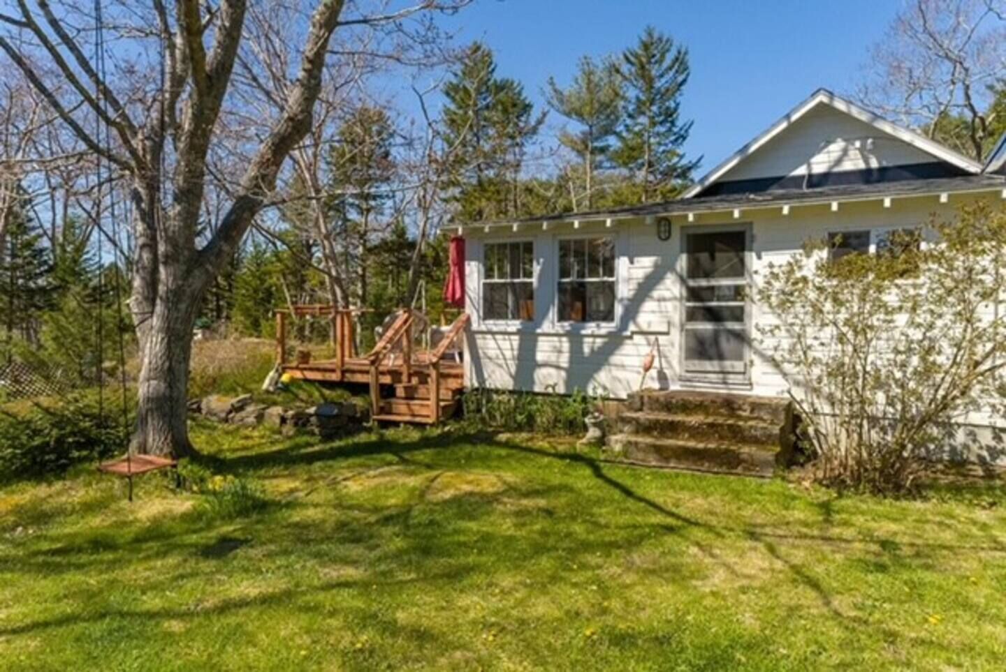 A white house with a porch, a swing set, and a small deck.
