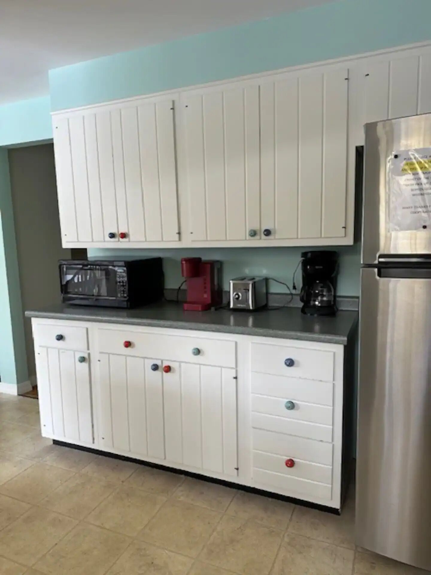 A kitchen with white cabinets, a microwave, a toaster, a coffee maker, and a refrigerator.