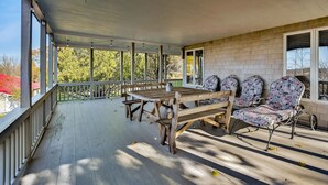 A covered outdoor patio with a wooden table and floral chairs, surrounded by a white railing and large windows. - Orr's Island Ocean Views (Orr's Island)
