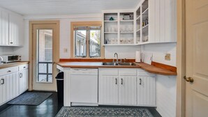 A compact kitchen with white cabinetry, a wooden countertop, a built-in wine rack, and a dishwasher. - Orr's Island Ocean Views (Orr's Island)