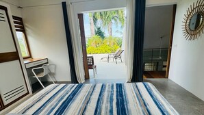 Ein Schlafzimmer mit Bett, Schreibtisch und Stuhl. Ein Balkon mit Blick auf Grünflächen und einem Stuhl davor.