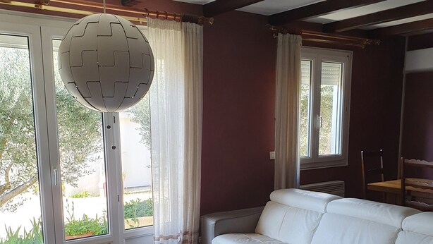 Un salon avec un canapé blanc, un pouf rond et un luminaire suspendu au plafond.