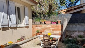 Un espace patio aménagé avec une table et des chaises, entouré de plantes en pot et d’un mur en briques.