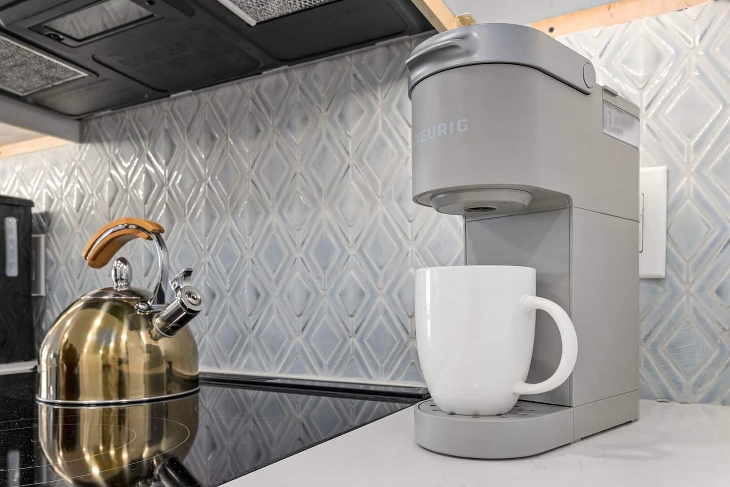 A modern kitchen with a kettle, a coffee maker, and a white mug on a countertop.