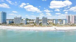 Et strandhotel med flere høje bygninger, en sandstrand og klare blå himmel.