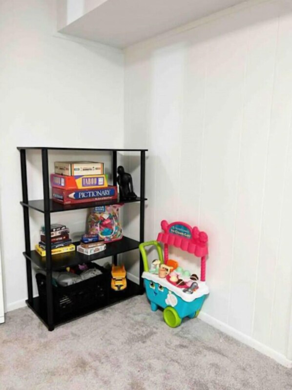 Habitación de esquina con una estantería negra contra la pared, que contiene varios juguetes y juegos.
