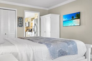 A bedroom with a bed, a wardrobe, a kitchen visible through an open door, and a beach scene on the wall.