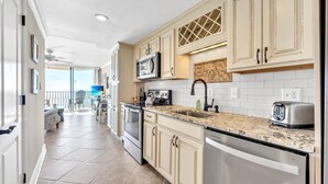 A modern kitchen with beige cabinetry, a granite countertop, stainless steel appliances, and a view to a balcony. - Direct Ocean Front w/washer and dryer! (Myrtle Beach)