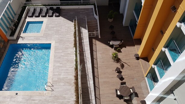 Ein Poolbereich auf dem Dach mit einem rechteckigen Pool, Liegestühlen und einem kleinen Tisch mit Stühlen.