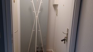 Ein schmaler Flur mit Kleiderhaken, einer Tür mit Griff und einer kleinen Fußmatte.