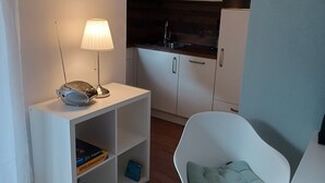 Eine kompakte Küche mit weißen Schränken, einem eingebauten Herd und einer kleinen Essecke mit einem weißen Stuhl und einem Tisch.