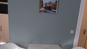 Ein modernes Zimmer mit einem weißen Tisch und zwei weißen Stühlen, einem gerahmten Bild an der Wand und einer Tür rechts.
