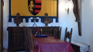 A dining area with a table set for four, wooden chairs, a red tablecloth, a wooden ceiling, a flag with a coat of arms, and a crucifix on the wall. - Casa Serafina Typical Three-room Apartment Historic Green Area (Orvieto)