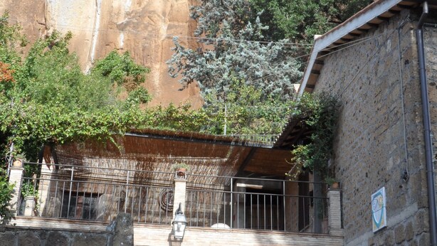 A stone building with a balcony, a car parked in front, and a rocky cliff in the background. - Casa Serafina Typical Three-room Apartment Historic Green Area (Orvieto)