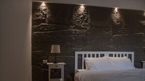 A bedroom with a stone wall, a white bed, and a nightstand with a lamp. - Saraya Locanda (Salt)