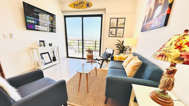 A modern living room with a sofa, armchair, and coffee table. A large window offers a view of the city. - CASA JOY  
Beautifuly decorated, Great location & Perfect escape to los Cabos.
 (Cabo San Lucas)