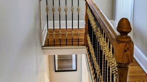 Una escalera con barandilla de madera y balaustradas negras, un espejo redondo en la pared y una rejilla de ventilación en el techo.