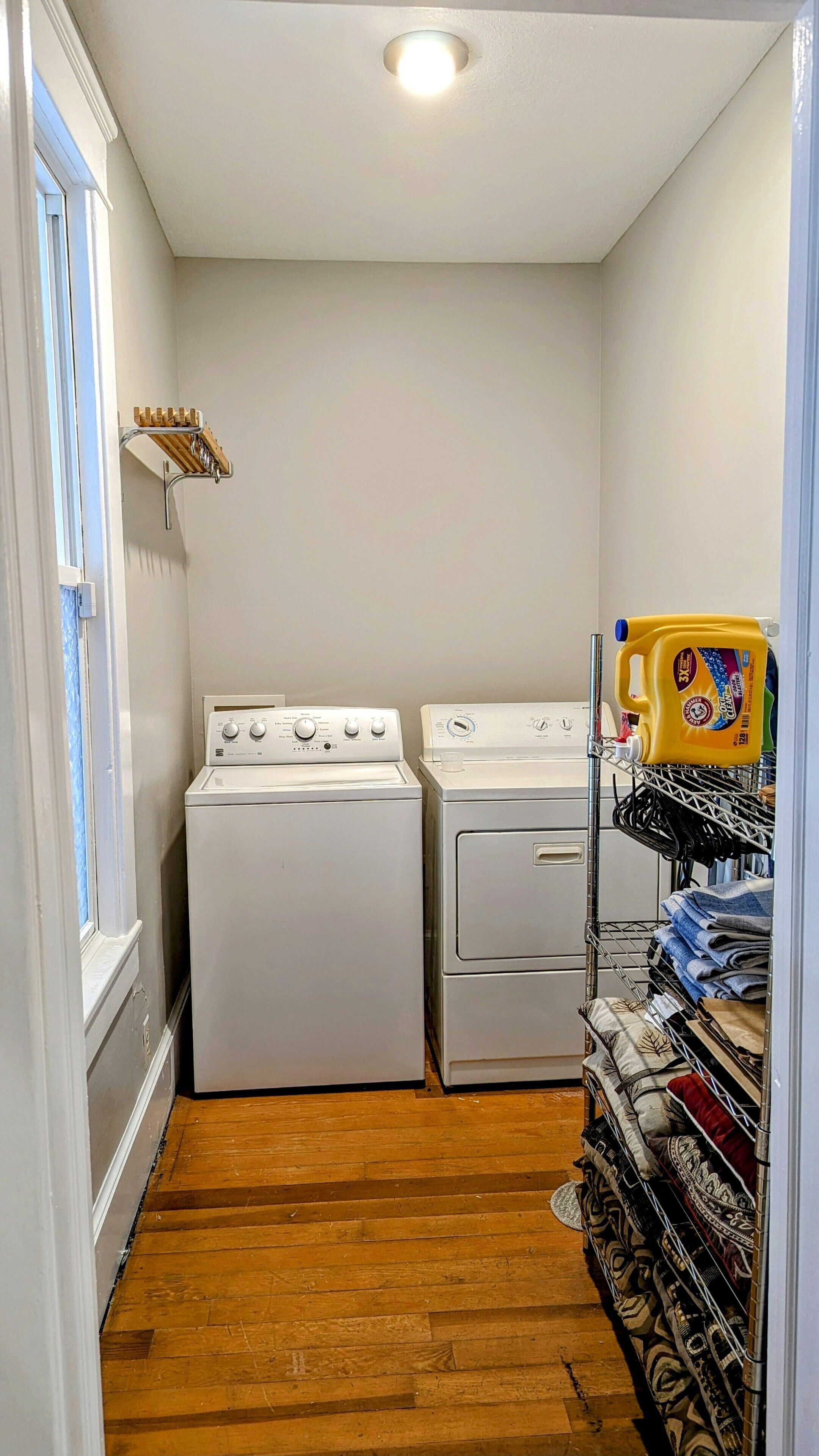 A laundry room with two stacked washers and dryers, a drying rack, and a shelf with laundry supplies.