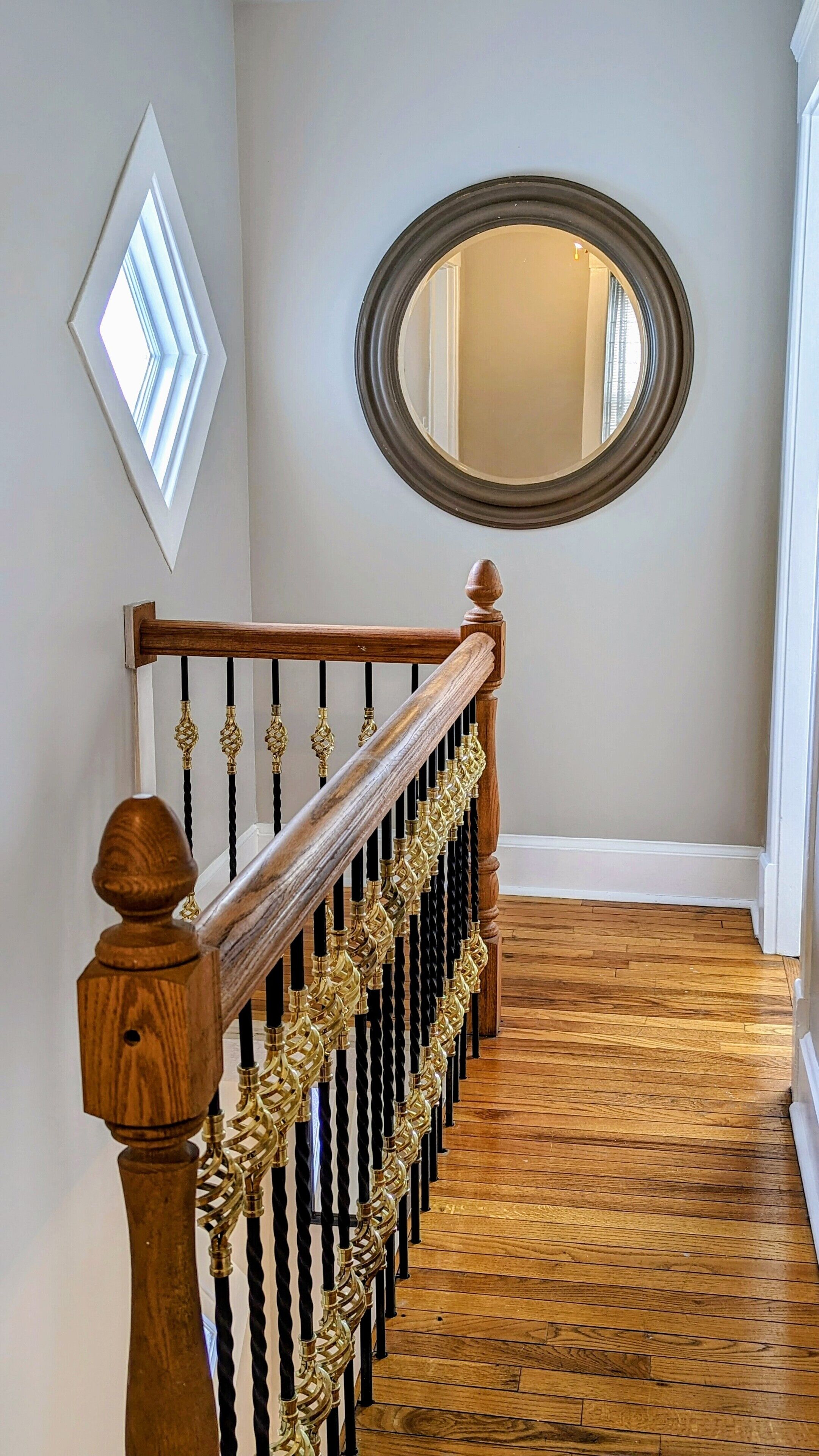A wooden staircase with a balustrade, a round mirror on the wall, and a diamond-shaped light fixture.