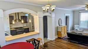 Una cocina compacta con una isla integrada, una zona de comedor con una silla roja y una sala de estar con un sillón blanco.