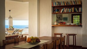 Een eetruimte met een houten tafel, stoelen, een schaal fruit en een boekenkast.
