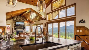 Une cuisine spacieuse dotée d’un grand îlot central, d’une cheminée en pierre et offrant une vue sur les montagnes grâce à de larges fenêtres.