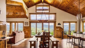 Une cuisine spacieuse avec des plans de travail en bois, un coin repas avec une table et des bancs en bois, et de grandes fenêtres offrant une vue sur les montagnes.