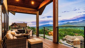 Une terrasse en bois, meublée de meubles en osier, avec vue sur un paysage montagneux.