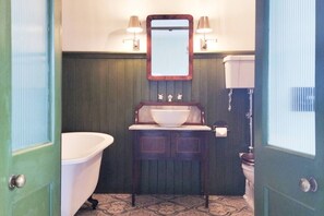 A bathroom with a white bathtub, a wooden vanity with a sink, and a mirror above the sink. - The Old Kirk and Manse, Hollymount (Hollymount)