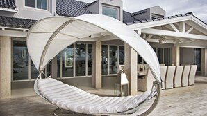 A modern outdoor seating area with a swing chair and a dining table. - Villa C’est La Vie – Luxury Beachfront Villa on Plum Bay, St. Martin with Private Chef (Marigot)