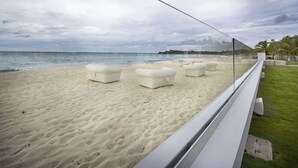 A beach with white cushioned seating and a glass barrier overlooking the ocean. - Villa C’est La Vie – Luxury Beachfront Villa on Plum Bay, St. Martin with Private Chef (Marigot)