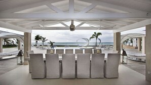 A covered outdoor seating area with a view of the ocean, featuring a table with chairs and a hanging light fixture. - Villa C’est La Vie – Luxury Beachfront Villa on Plum Bay, St. Martin with Private Chef (Marigot)