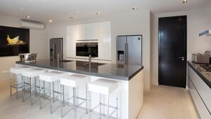 A modern kitchen with a central island, bar stools, stainless steel appliances, and a black door. - The Pearl of Jan Thiel 1 – Luxury Designer Villa with Private Pool & Resort Facilities in Curaçao (Willemstad)