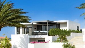 A modern two-story house with a balcony, surrounded by greenery and flowers. - The Pearl of Jan Thiel 1 – Luxury Designer Villa with Private Pool & Resort Facilities in Curaçao (Willemstad)