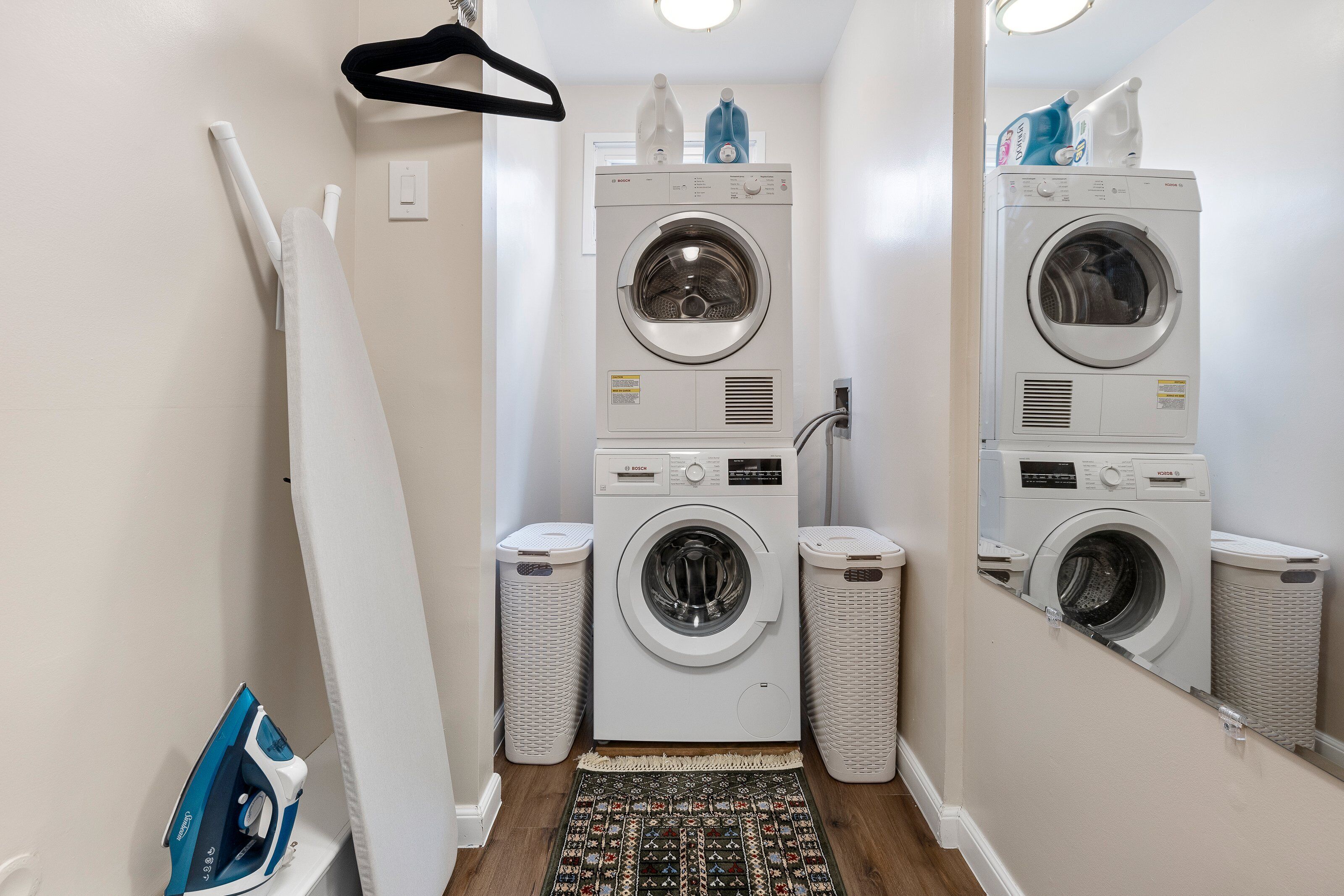 Une petite buanderie équipée de deux machines à laver superposées, d’un étendoir et de deux poubelles.