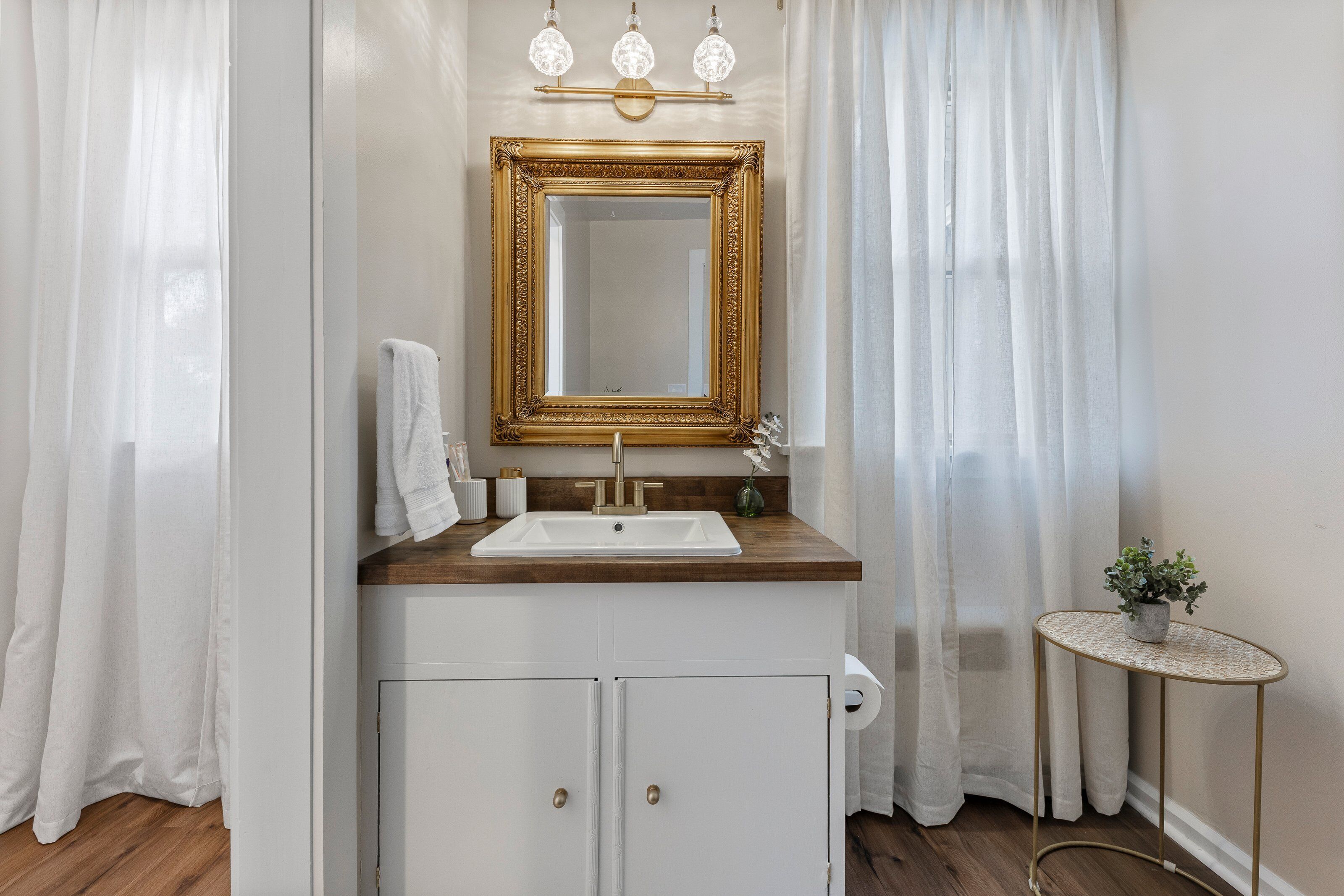 A bathroom with a white sink, gold-framed mirror, and a small round table with a plant.