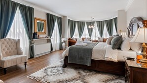 A spacious bedroom with a large bed, a sitting area with a chair, a vanity with a mirror, and a chandelier. - - Beautiful Condo - King Bed - Free Waffle Breakfast - (Geneva)