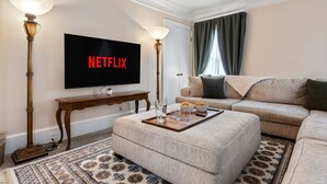 A living room with a flat-screen TV displaying "NETFLIX," a beige sofa, a coffee table with snacks, and a patterned rug. - - Beautiful Condo - King Bed - Free Waffle Breakfast - (Geneva)