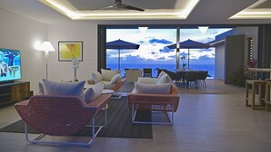 A modern living room with a large TV, comfortable seating, and a view of the ocean.